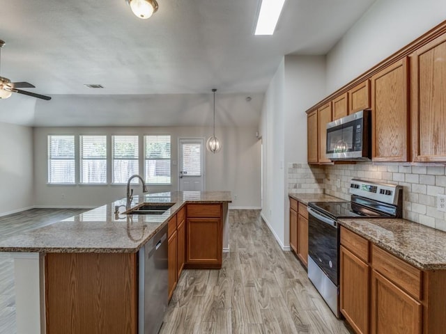 kitchen with appliances with stainless steel finishes, light wood-type flooring, a center island with sink, and sink