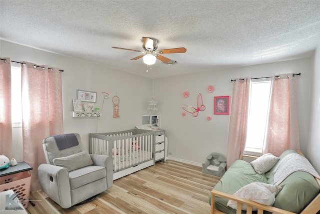 bedroom featuring a textured ceiling, ceiling fan, light hardwood / wood-style floors, and a crib