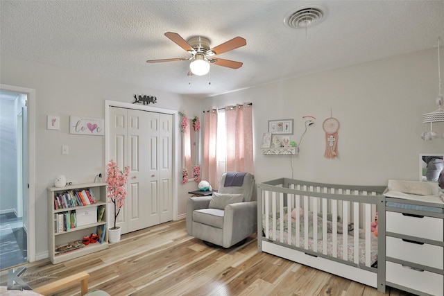 bedroom featuring ceiling fan, a textured ceiling, light hardwood / wood-style floors, a crib, and a closet