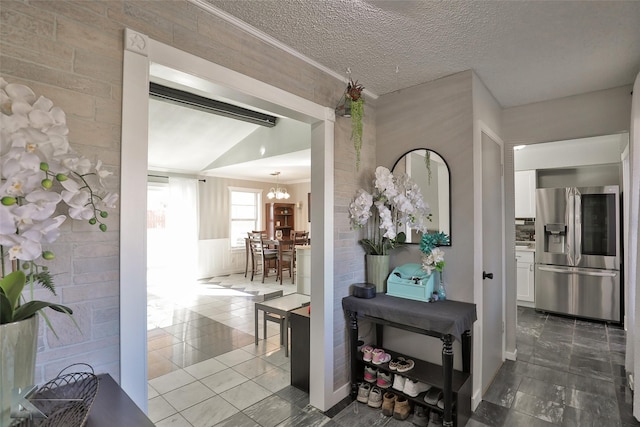 hall featuring tile patterned flooring, a chandelier, a textured ceiling, and ornamental molding