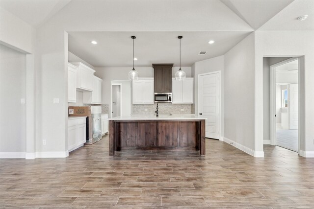 kitchen featuring white cabinetry, hanging light fixtures, backsplash, an island with sink, and lofted ceiling