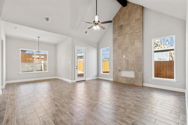 unfurnished living room with ceiling fan with notable chandelier, a healthy amount of sunlight, beam ceiling, and high vaulted ceiling