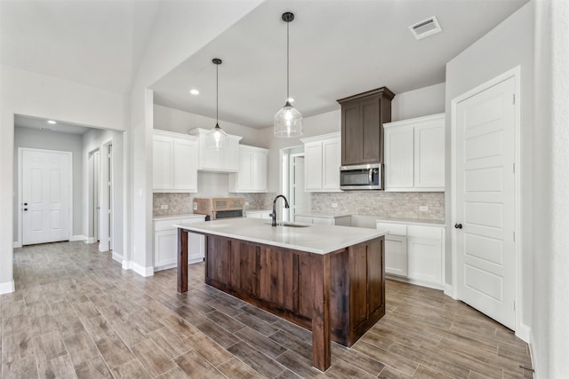 kitchen with a kitchen island with sink, white cabinets, hanging light fixtures, sink, and dark brown cabinets