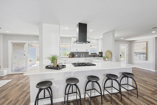 kitchen with island range hood, kitchen peninsula, a breakfast bar area, and white cabinetry