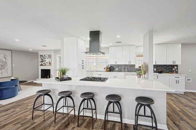 kitchen featuring dark hardwood / wood-style flooring, range hood, a breakfast bar area, a fireplace, and white cabinets