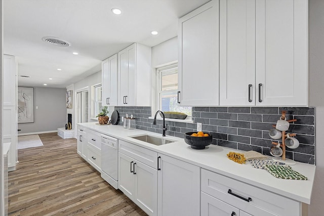 kitchen with sink, tasteful backsplash, white dishwasher, white cabinets, and hardwood / wood-style flooring