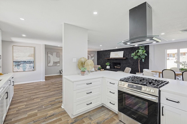 kitchen featuring kitchen peninsula, island range hood, wood-type flooring, white cabinets, and stainless steel range with gas stovetop