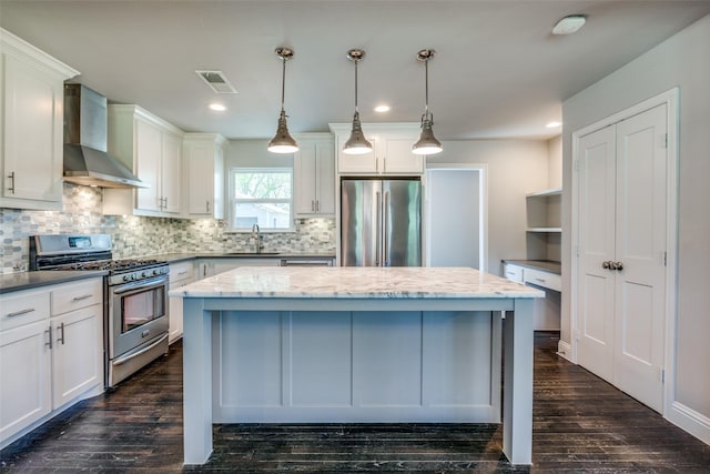 kitchen featuring visible vents, wall chimney exhaust hood, appliances with stainless steel finishes, a center island, and a sink