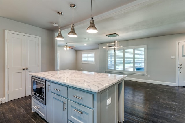 kitchen with dark wood-type flooring, decorative light fixtures, stainless steel microwave, a kitchen island, and ceiling fan