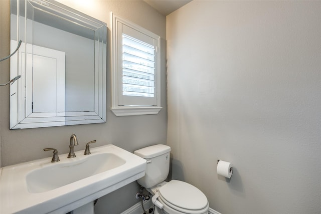 half bath featuring a sink, toilet, and baseboards