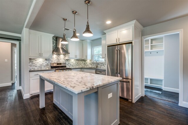 kitchen featuring appliances with stainless steel finishes, a kitchen island, white cabinetry, wall chimney range hood, and hanging light fixtures