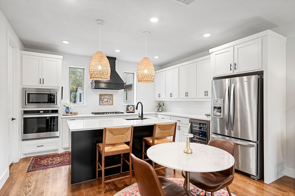 kitchen featuring wine cooler, sink, hanging light fixtures, a center island with sink, and stainless steel appliances