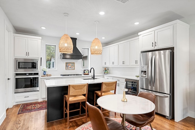 kitchen with sink, beverage cooler, an island with sink, decorative light fixtures, and appliances with stainless steel finishes