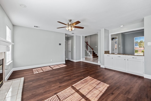 unfurnished living room featuring a tile fireplace, dark hardwood / wood-style floors, and ceiling fan