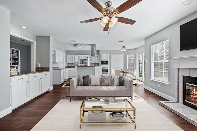 living room featuring ceiling fan, dark hardwood / wood-style flooring, plenty of natural light, and a tiled fireplace