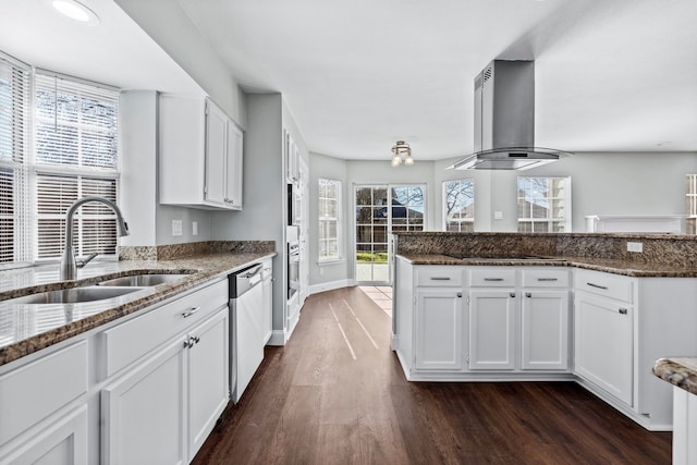 kitchen with stainless steel dishwasher, dark stone counters, sink, exhaust hood, and white cabinets