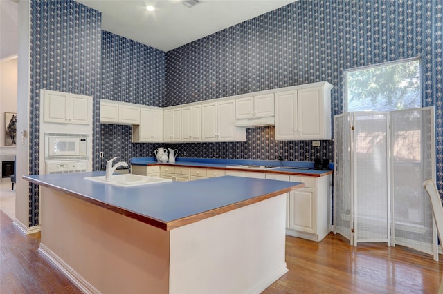 kitchen featuring light wood-type flooring, white appliances, sink, a center island with sink, and white cabinetry