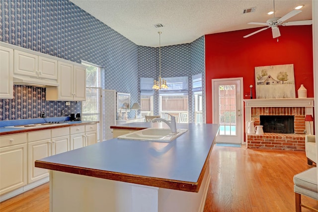 kitchen featuring a fireplace, decorative light fixtures, a center island with sink, and light hardwood / wood-style floors