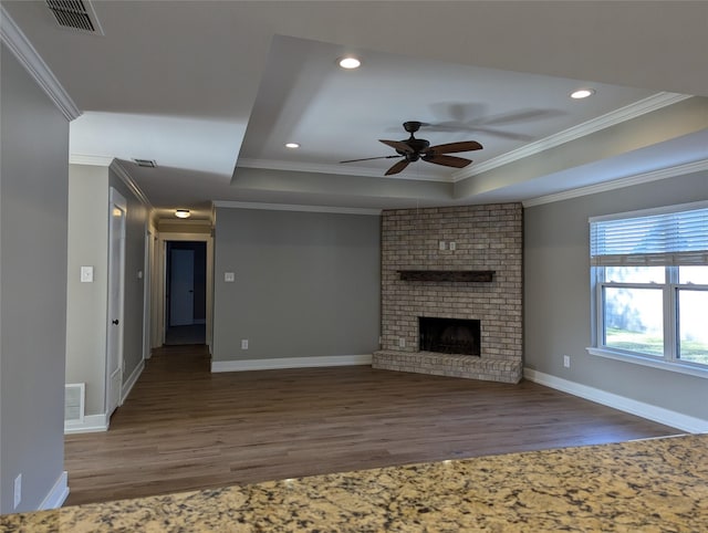 unfurnished living room with dark hardwood / wood-style flooring, ornamental molding, a tray ceiling, ceiling fan, and a fireplace