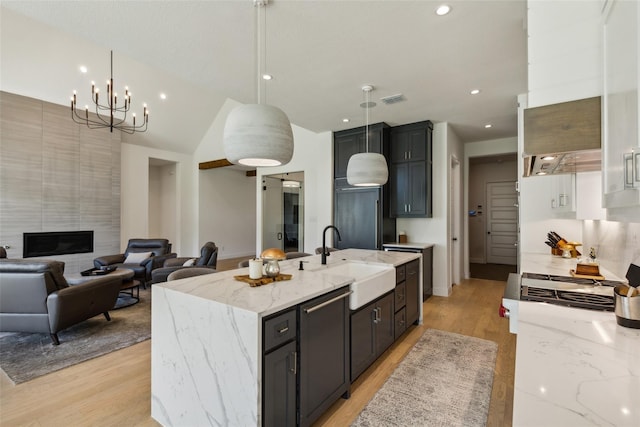 kitchen featuring a high end fireplace, a center island with sink, sink, decorative light fixtures, and light stone counters