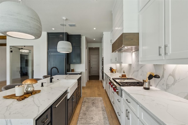 kitchen with a center island with sink, sink, decorative backsplash, decorative light fixtures, and white cabinetry