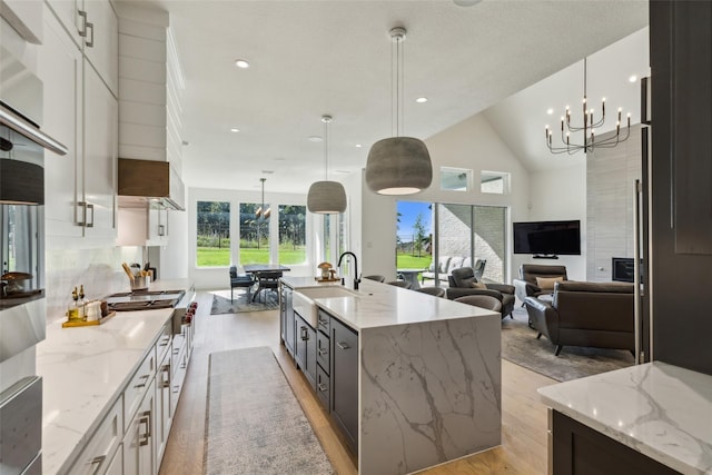 kitchen with white cabinets, sink, hanging light fixtures, light stone countertops, and a large island