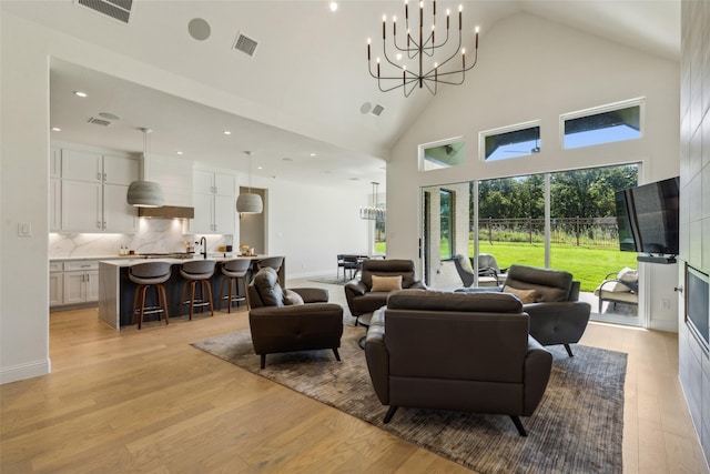 living room featuring a towering ceiling, light hardwood / wood-style floors, and an inviting chandelier