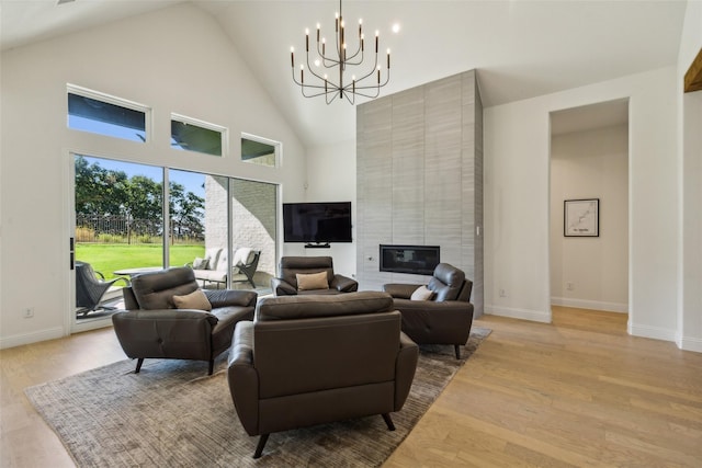 living room with an inviting chandelier, a high ceiling, a tile fireplace, and light hardwood / wood-style flooring