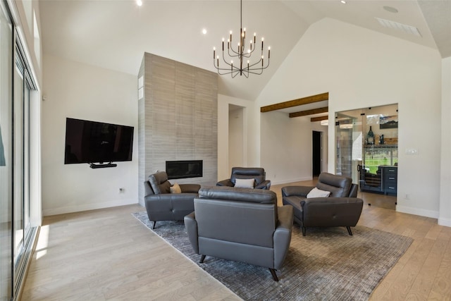 living room with light hardwood / wood-style flooring, a high ceiling, a tile fireplace, and a chandelier