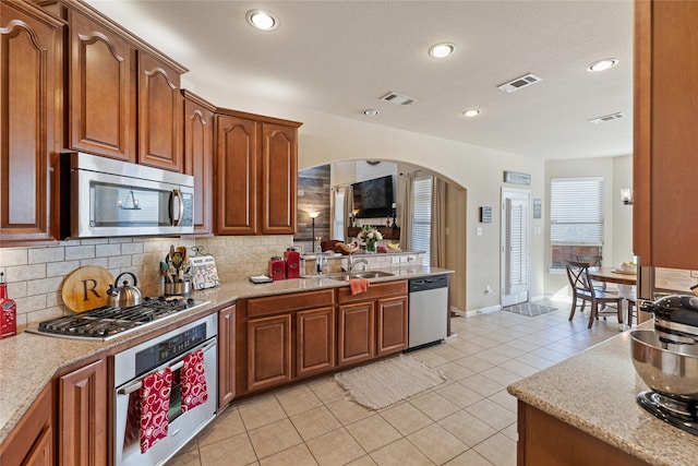 kitchen with sink, light stone counters, backsplash, light tile patterned floors, and appliances with stainless steel finishes