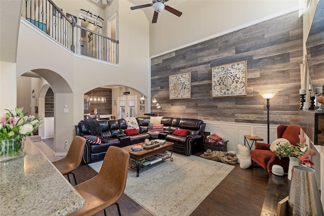 living room with wood walls, a towering ceiling, ceiling fan, and hardwood / wood-style floors