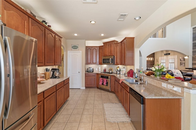 kitchen with kitchen peninsula, appliances with stainless steel finishes, backsplash, light stone countertops, and sink