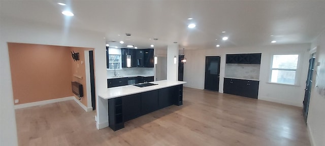 kitchen with pendant lighting, sink, a kitchen island, and light wood-type flooring