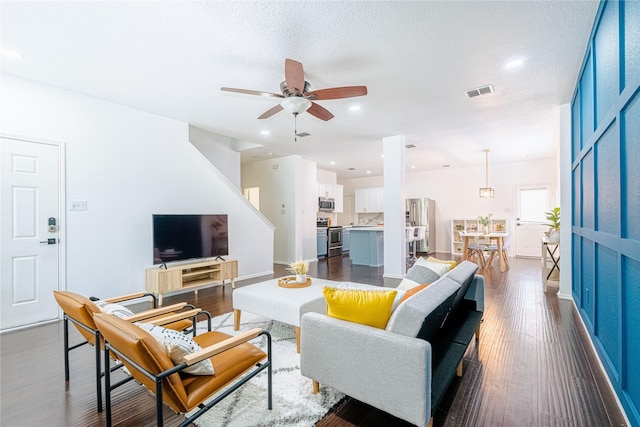 living room featuring a textured ceiling, ceiling fan, and dark wood-type flooring