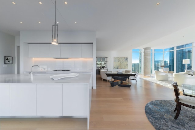 kitchen with white cabinetry, sink, pendant lighting, a center island with sink, and light wood-type flooring