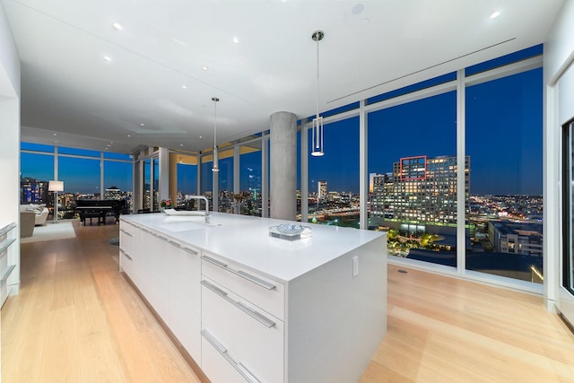 kitchen with sink, hanging light fixtures, light hardwood / wood-style flooring, a kitchen island with sink, and white cabinets