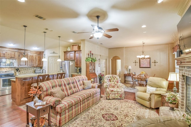 living room with vaulted ceiling, ornamental molding, light hardwood / wood-style floors, a fireplace, and ceiling fan with notable chandelier