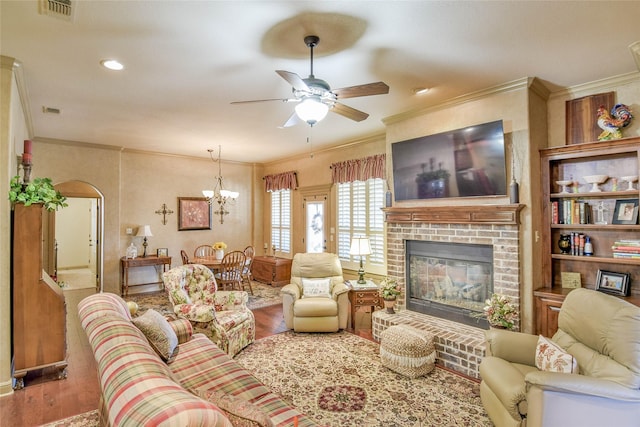 living room featuring hardwood / wood-style flooring, a fireplace, crown molding, and ceiling fan with notable chandelier