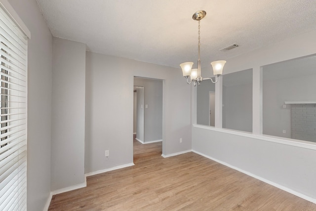 empty room featuring a chandelier, a textured ceiling, and light wood-type flooring