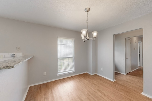 unfurnished dining area with an inviting chandelier, light hardwood / wood-style floors, and a textured ceiling