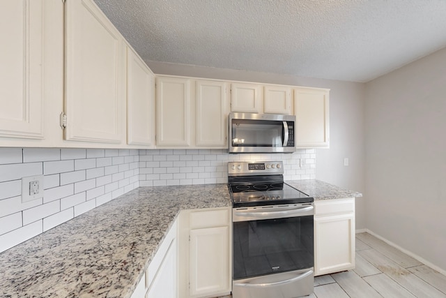 kitchen featuring light stone counters, a textured ceiling, stainless steel appliances, light hardwood / wood-style floors, and decorative backsplash