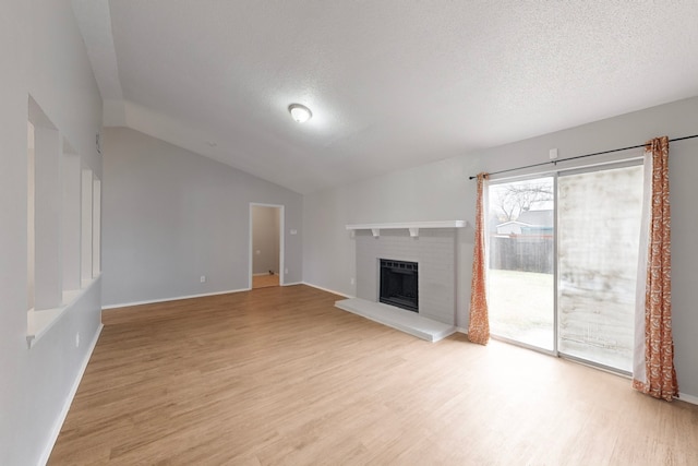 unfurnished living room with lofted ceiling, a brick fireplace, light hardwood / wood-style floors, and a textured ceiling