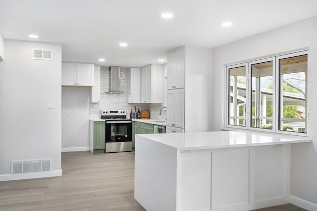 kitchen with stainless steel electric range oven, wall chimney range hood, green cabinets, decorative backsplash, and white cabinets