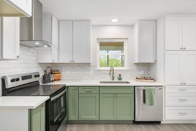 kitchen featuring white cabinets, wall chimney range hood, sink, green cabinetry, and stainless steel appliances