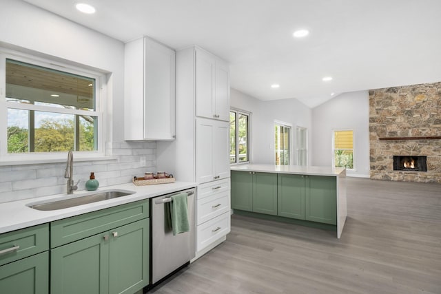 kitchen with backsplash, stainless steel dishwasher, sink, white cabinets, and a stone fireplace