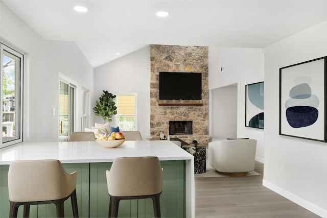 kitchen featuring kitchen peninsula, a breakfast bar area, light hardwood / wood-style floors, a stone fireplace, and green cabinets