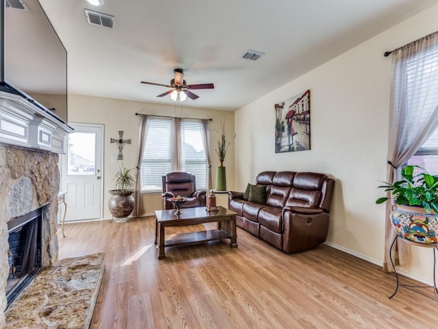 living room featuring ceiling fan, light hardwood / wood-style floors, and a stone fireplace