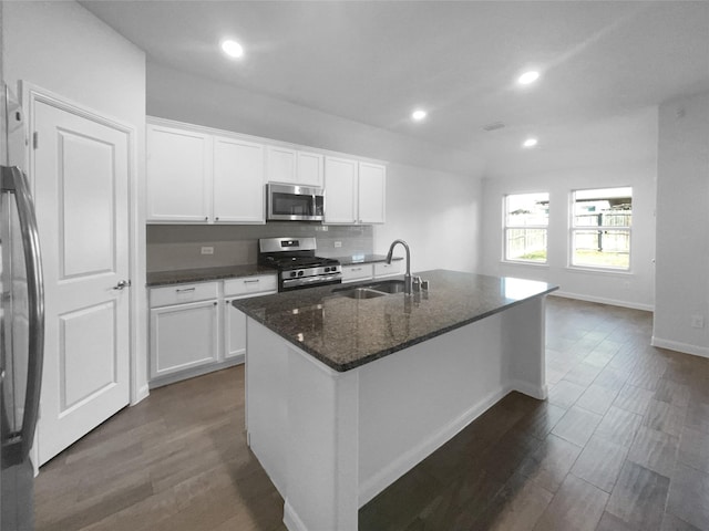 kitchen featuring sink, appliances with stainless steel finishes, white cabinetry, an island with sink, and dark stone counters