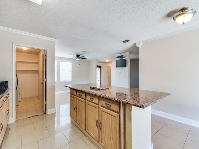 kitchen with a center island, dark stone counters, ceiling fan, ornamental molding, and light tile patterned floors