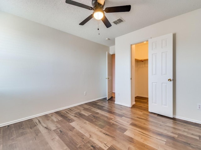 unfurnished bedroom featuring hardwood / wood-style flooring, ceiling fan, a walk in closet, and a closet